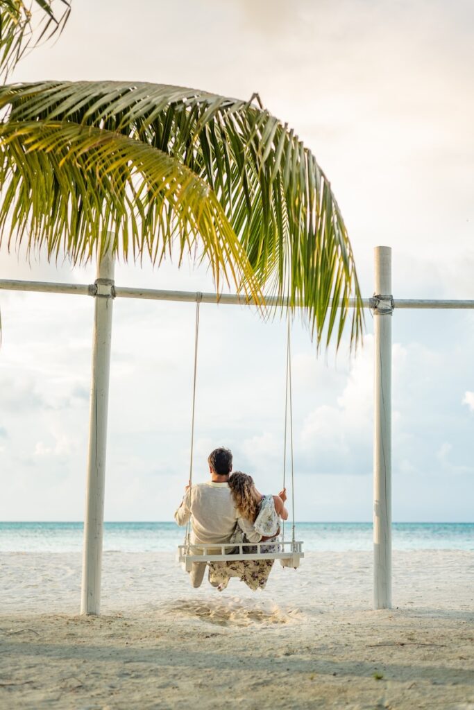 man in white shirt sitting on swing chair under coconut tree during daytime